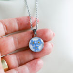 Ogrlica s spominčicami prikazana na roki.