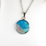 Ročno izdelana okrogla ogrlica z modro zelenim medaljonom in peskom iz reke Soče, premera 22 mm – darilo za ljubiteljico narave.