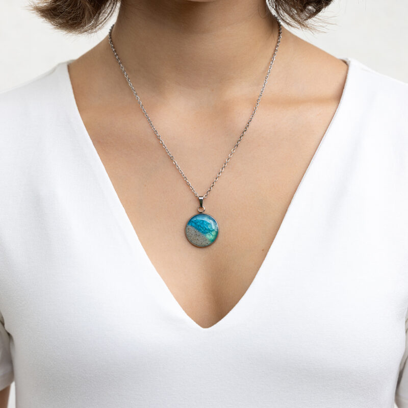 Ročno izdelana okrogla ogrlica z modro zelenim medaljonom in peskom iz reke Soče, premera 22 mm – darilo za ljubiteljico narave.