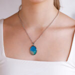 Ovalna ogrlica iz kolekcije Soča z modro-zelenim motivom in peskom iz reke Soče, na modelu