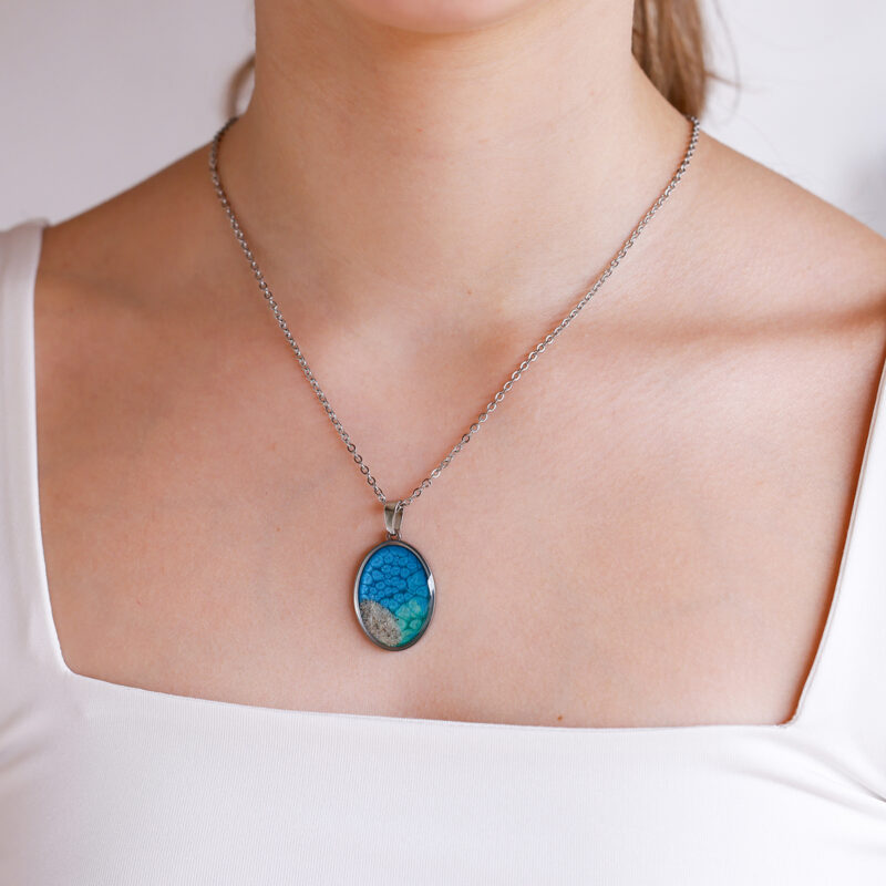 Ovalna ogrlica iz kolekcije Soča z modro-zelenim motivom in peskom iz reke Soče, na modelu