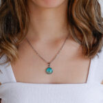 Ogrlica iz kolekcije Soča z majhnim okroglim obeskom turkizno zelene barve in peskom iz reke Soče, prikazana na modelu.