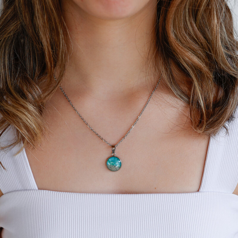 Ogrlica iz kolekcije Soča z majhnim okroglim obeskom turkizno zelene barve in peskom iz reke Soče, prikazana na modelu.