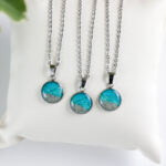 Ogrlice z okroglim obeskom v turkizno zeleni barvi in peskom iz reke Soče na srebrni verižici iz nerjavečega jekla – kolekcija Soča.