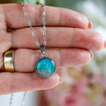 Ogrlice z okroglim obeskom v turkizno zeleni barvi in peskom iz reke Soče na srebrni verižici iz nerjavečega jekla – kolekcija Soča.