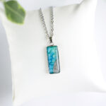 Ročno izdelana ogrlica pravokotne oblike z modro-zeleno poslikavo in pravim peskom iz reke Soče, unikatni kos nakita iz Slovenije.