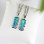 Ročno izdelana ogrlica pravokotne oblike z modro-zeleno poslikavo in pravim peskom iz reke Soče na blazinici