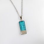 Ogrlica Soča, pravokotna oblika, turkizna, z drobnim peskom iz reke Soče, ročno izdelana iz nerjavečega jekla.
