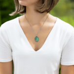 Ogrlica z ovalnim zelenim medaljonom, peskom iz reke Soče in sijočo smolo – ročno izdelano darilo za ljubiteljice narave. Prikaz na modelu.