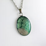 Ogrlica z ovalnim zelenim medaljonom, peskom iz reke Soče in sijočo smolo – ročno izdelano darilo za ljubiteljice narave.
