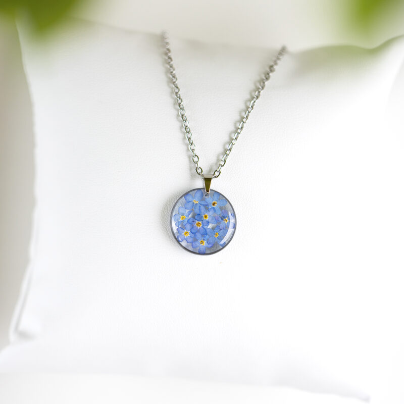 Ogrlica s pravimi cvetovi spominčic v okroglem medaljonu iz prozorne smole, na verižici iz nerjavečega jekla.