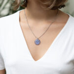 Ogrlica s pravimi cvetovi spominčic v okroglem medaljonu iz prozorne smole, na verižici iz nerjavečega jekla. Prikaz na ženskem vratu.