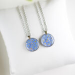 Ogrlica s pravimi cvetovi spominčic v okroglem medaljonu iz prozorne smole, na verižici iz nerjavečega jekla.