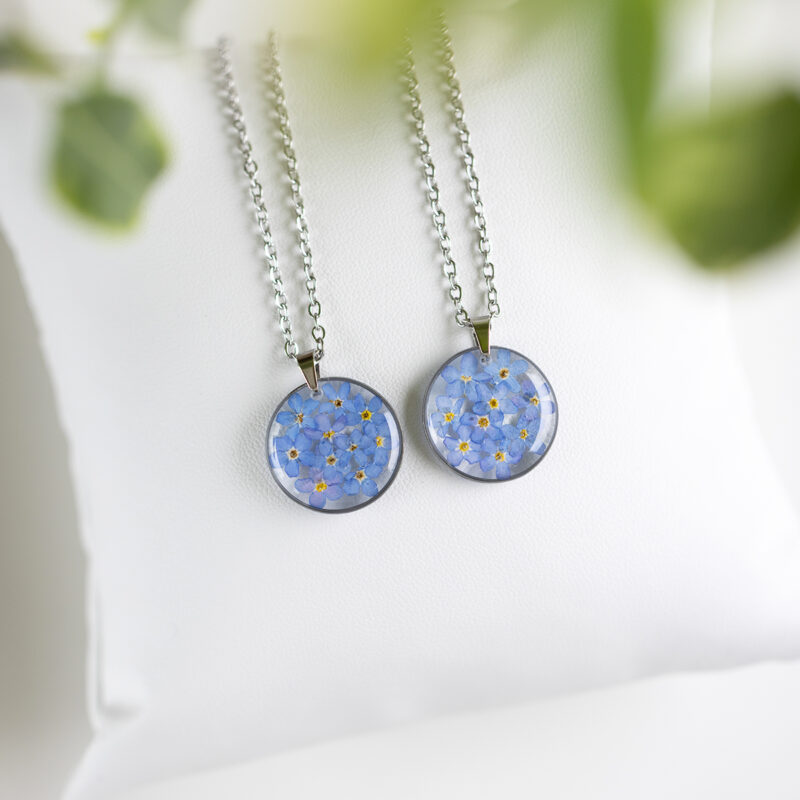 Ogrlica s pravimi cvetovi spominčic v okroglem medaljonu iz prozorne smole, na verižici iz nerjavečega jekla.