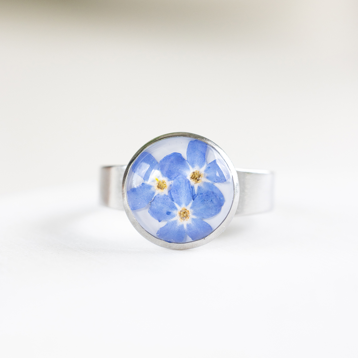 prstan-spomincice-S-12mm (1) Ročno izdelan prstan iz nerjavečega jekla s pravimi posušenimi spominčicami in prozorno smolo – minimalističen kos z naravnim pridihom.