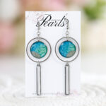 Unikatni viseči uhani Soča z modro-zelenim okroglim obeskom (16 mm) in peskom iz reke, dolžine 8 cm