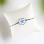 Zapestnica z nežno modro spominčico, ujeta v medaljon iz jekla, s tanko verižico iz nerjavečega jekla.