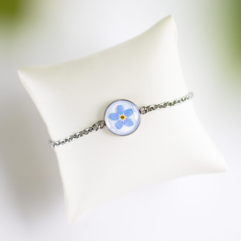 Zapestnica z nežno modro spominčico, ujeta v medaljon iz jekla, s tanko verižico iz nerjavečega jekla.