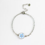 Zapestnica z nežno modro spominčico, ujeta v medaljon iz jekla, s tanko verižico iz nerjavečega jekla